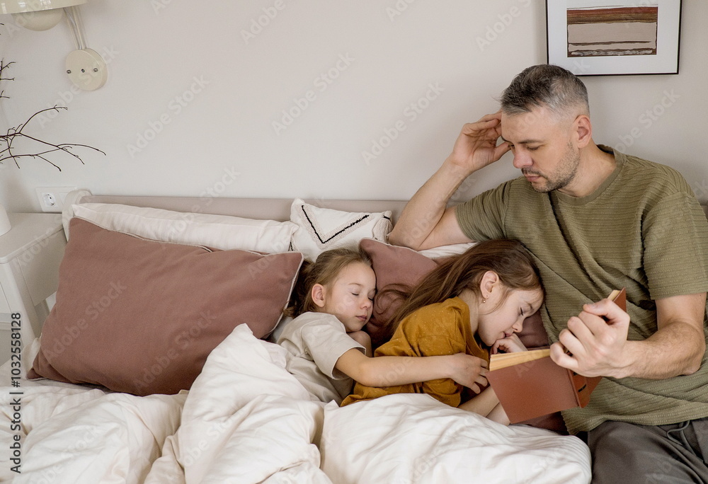 Fototapeta premium A father reads a bedtime story to his two daughters who are already asleep in bed.
