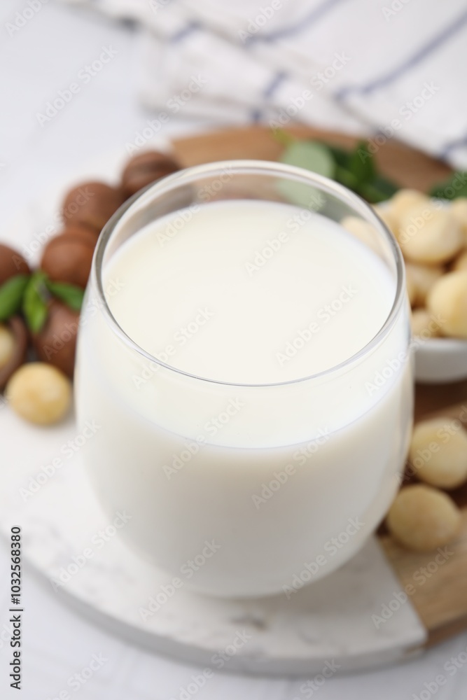 Glass of macadamia milk and nuts on white tiled table, closeup