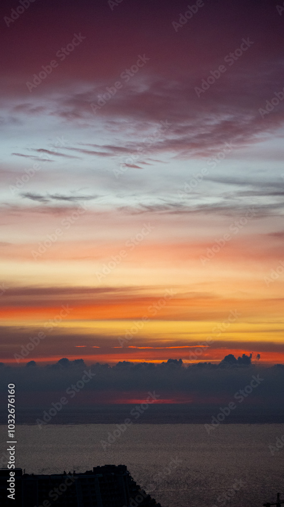 City skyline with buildings silhouetted against vibrant sunrise over the sea. Aerial view at dusk City skyline with buildings silhouetted against vibrant sunrise over the sea. Aerial view at dusk
