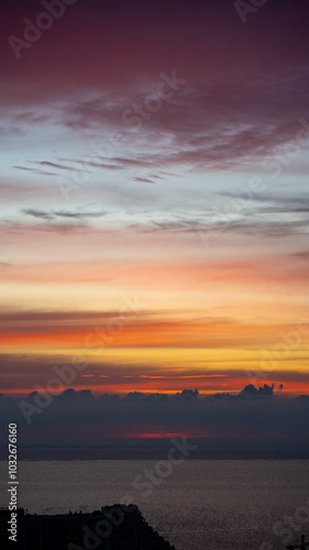 City skyline with buildings silhouetted against vibrant sunrise over the sea. Aerial view at dusk