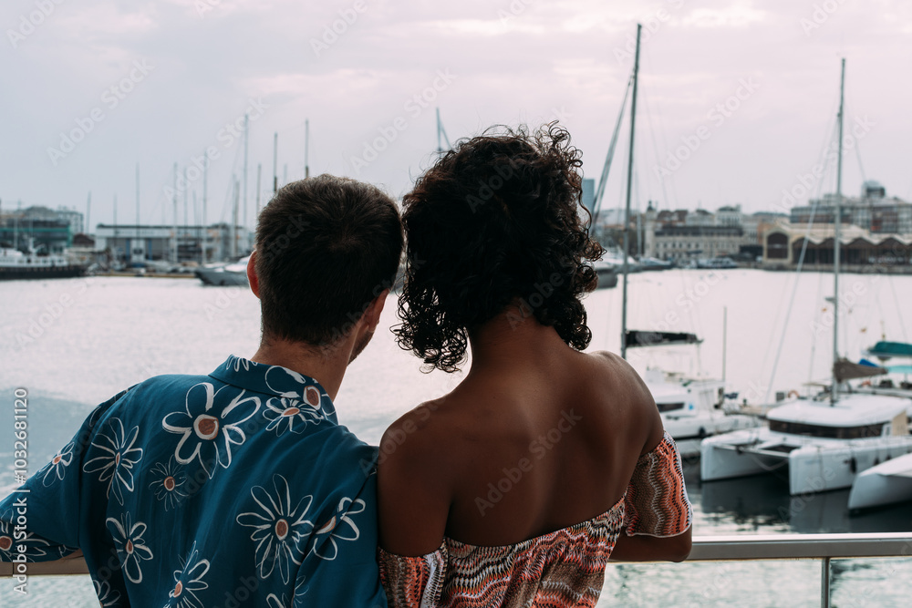 Fototapeta premium Young interracial couple relaxing on balcony overlooking marina.