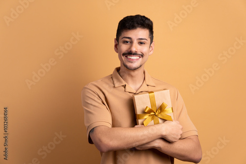 joyful brazilian man with gift box present in beige colors. christmas, happy birthday, celebration concept.