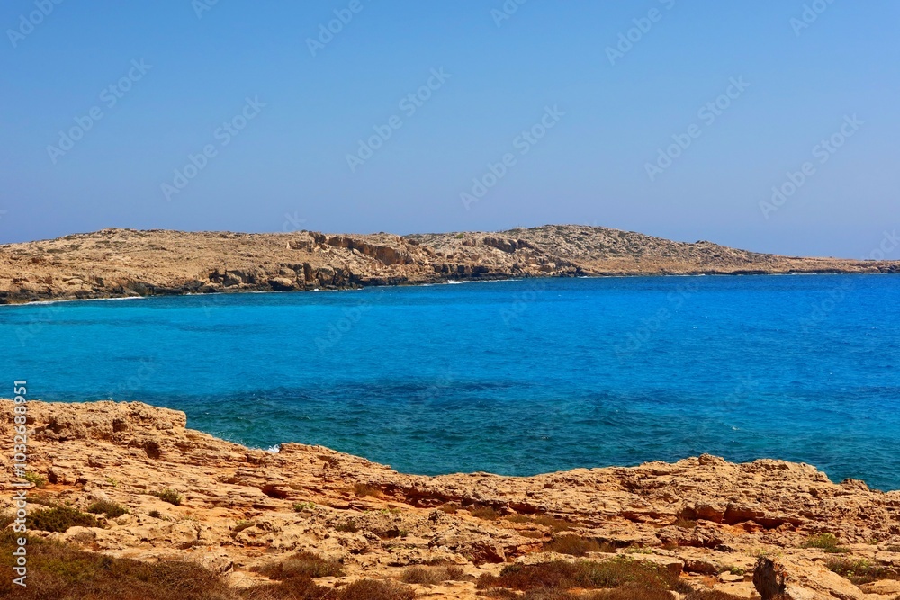 Empty bay and rocky shoreline, blue ocean water. Calm ocean, blue sky and sunny day. Horizon and sea, travel picture. Travel photo, adventure hike on the shore. Empty bay and rocky shoreline, blue ocean water. Calm ocean, blue sky and sunny day. Horizon and sea, travel picture. Travel photo, adventure hike on the shore.