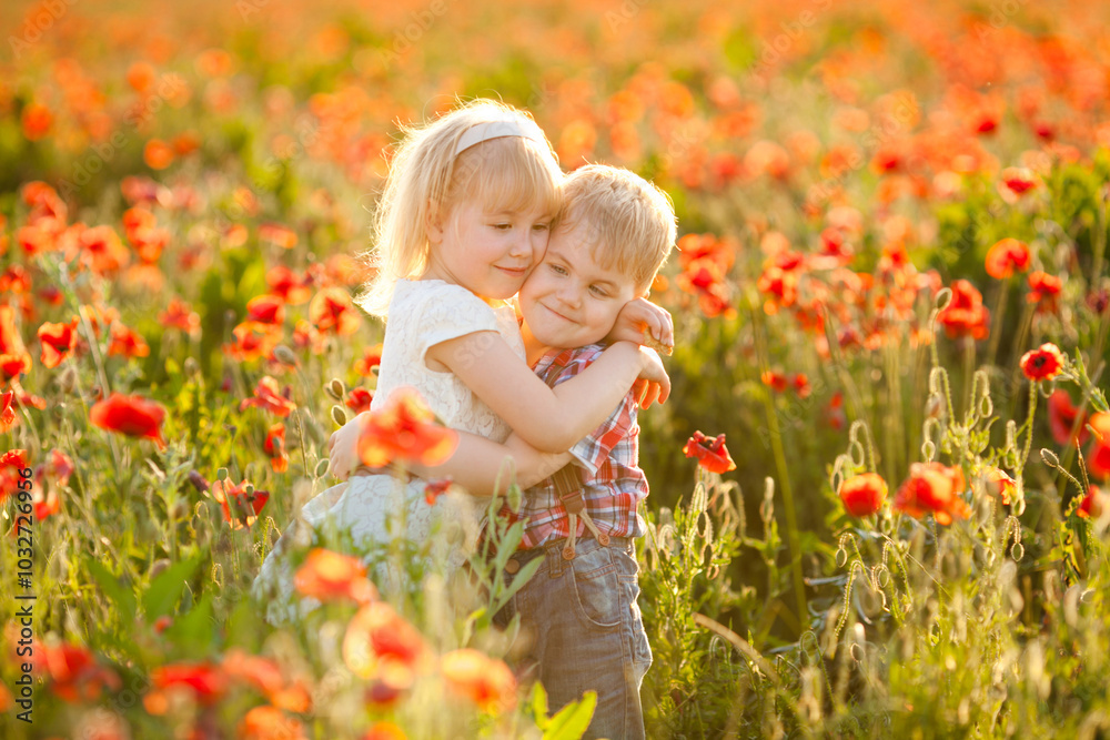Siblings with blonde hair share a close hug and smile in a poppy field at sunset in the summer