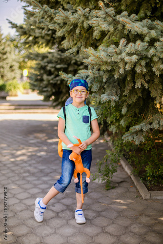 funny little boy in glasses, bandana, wearing a green t-shirt and denim shorts, having fun with a toy monkey