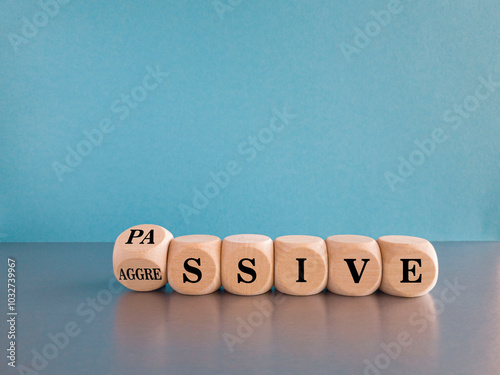 Passive or aggressive symbol. Turned a wooden cube and changes the word passive to aggressive. Beautiful gray table, blue background. Business concept.