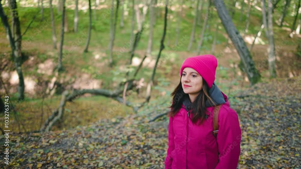 Attractive, positive young woman in a pink jacket, jeans and backpack walking through an autumn forest, slow motion Attractive, positive young woman in a pink jacket, jeans and backpack walking through an autumn forest, slow motion