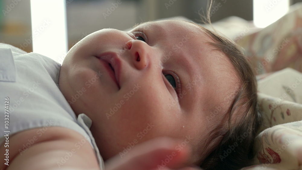 Baby lying on the bed, looking upwards with a faint smile. close-up view emphasizes the baby's cheeks and soft hair while the baby seems relaxed and content in the cozy setting Baby lying on the bed, looking upwards with a faint smile. close-up view emphasizes the baby's cheeks and soft hair while the baby seems relaxed and content in the cozy setting