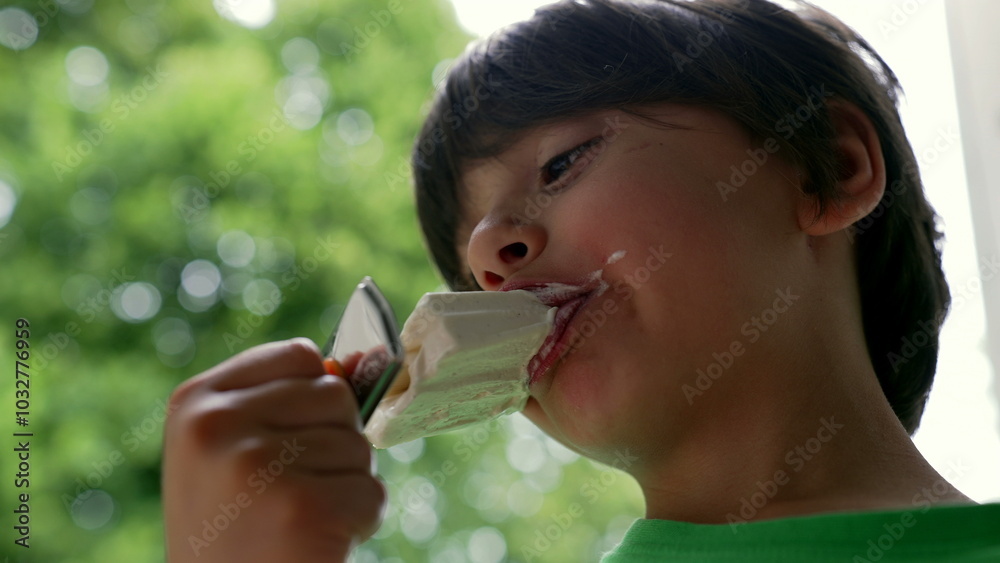 Child holding and observing an ice cream outdoors, enjoying a peaceful moment with a treat. Young boy focused on his snack in a green, natural environment Child holding and observing an ice cream outdoors, enjoying a peaceful moment with a treat. Young boy focused on his snack in a green, natural environment