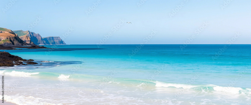 Obraz premium Serene ocean scene with clear blue waters gently lapping a sandy beach, with rugged cliffs in the distance. Ideal for themes of tranquility, natural beauty, relaxation, and coastal landscapes.