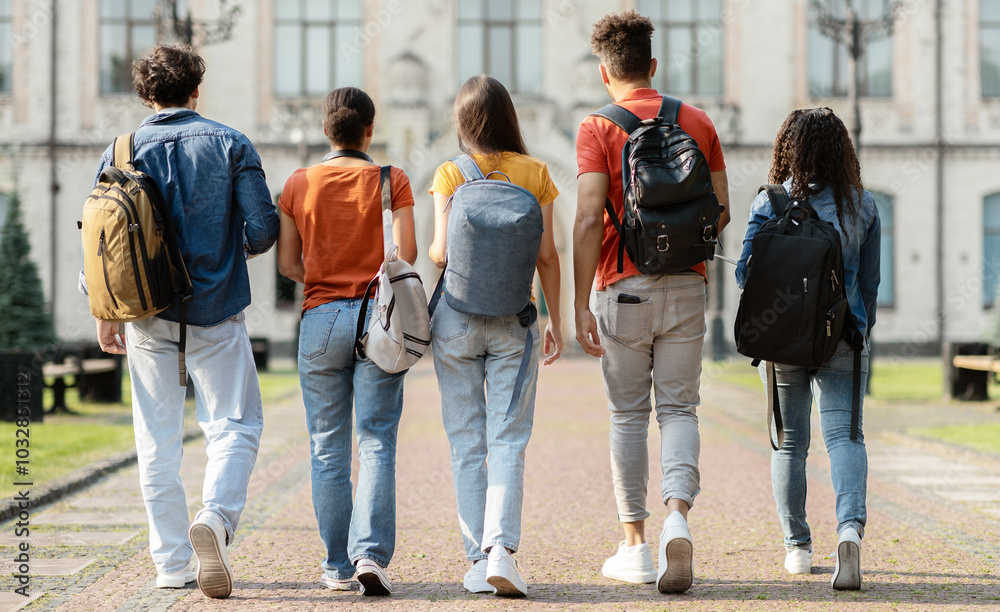 Obraz premium Group of five students with backpacks walking at university campus together, rear view of multiethnic young people going to classes, diverse college friends spending time outdoors after lessons