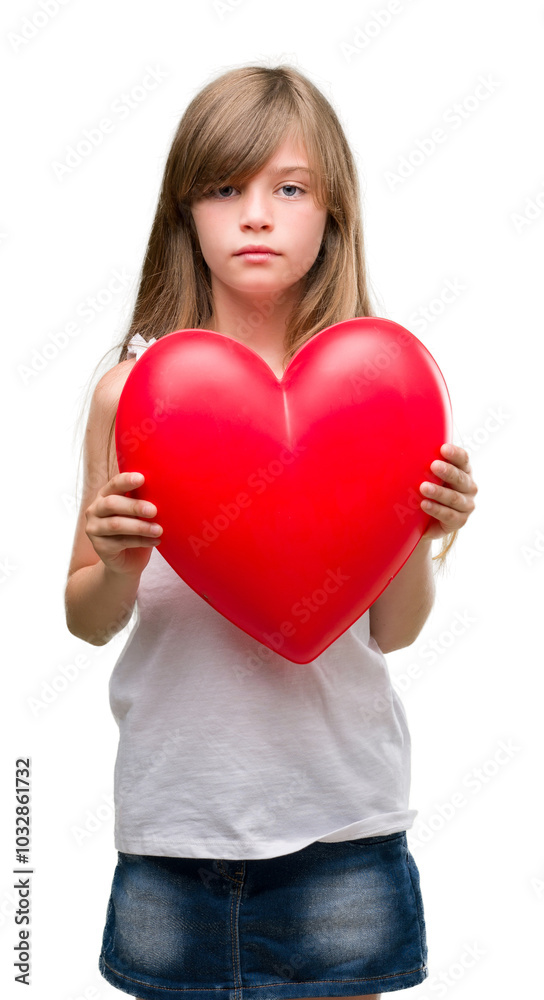 Young blonde toddler holding a red heart with a confident expression on smart face thinking serious Young blonde toddler holding a red heart with a confident expression on smart face thinking serious