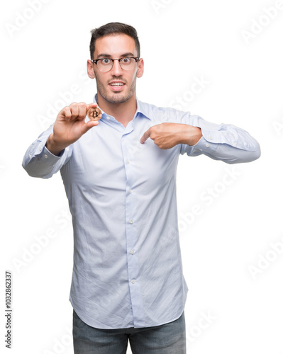 Handsome young man holding bitcoin with surprise face pointing finger to himself