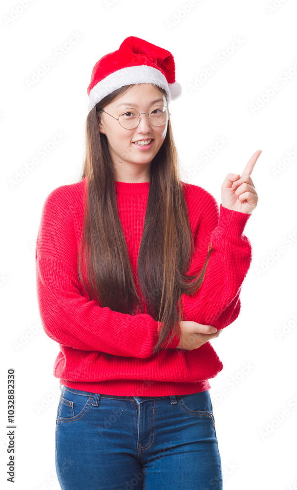 Young Chinese woman over isolated background wearing christmas hat with a big smile on face, pointing with hand and finger to the side looking at the camera. Young Chinese woman over isolated background wearing christmas hat with a big smile on face, pointing with hand and finger to the side looking at the camera.