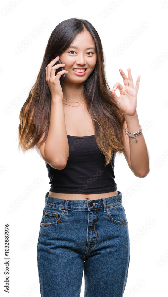 Young asian woman speaking on the phone over isolated background doing ok sign with fingers, excellent symbol Young asian woman speaking on the phone over isolated background doing ok sign with fingers, excellent symbol