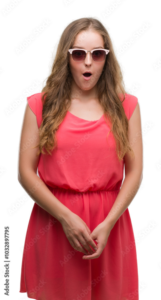 Young blonde woman wearing pink sunglasses scared in shock with a surprise face, afraid and excited with fear expression Young blonde woman wearing pink sunglasses scared in shock with a surprise face, afraid and excited with fear expression