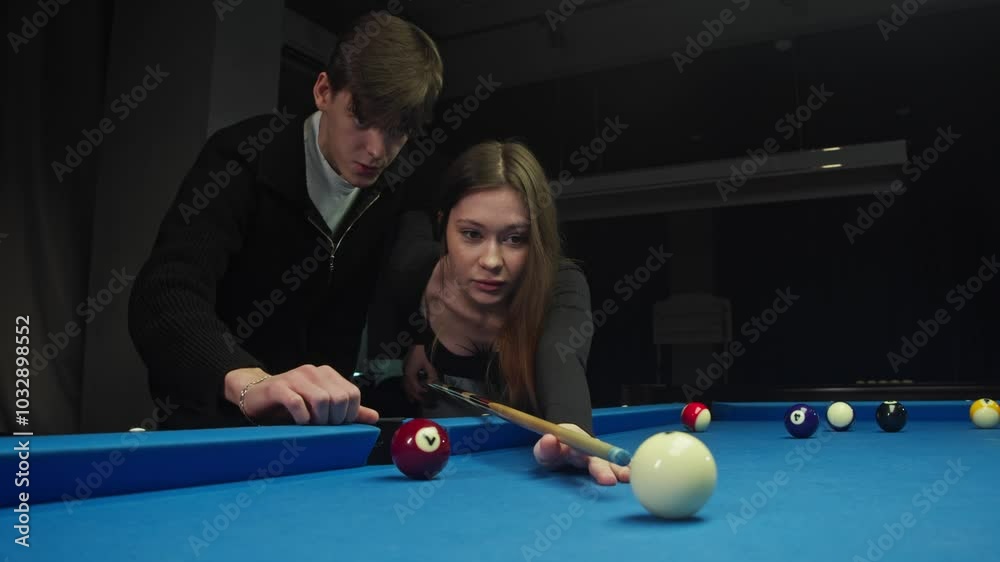 Young man teaches his beloved to play billiards. He talks in detail about rules of the American pool and helps her hold cue. In process of learning, he gently hugs her.