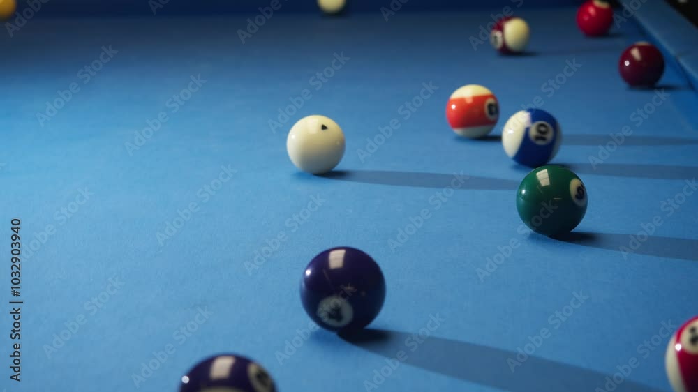 Multicolored American pool balls are scattered on billiard table covered with blue cloth. one of players makes a hit on white ball Multicolored American pool balls are scattered on billiard table covered with blue cloth. one of players makes a hit on white ball