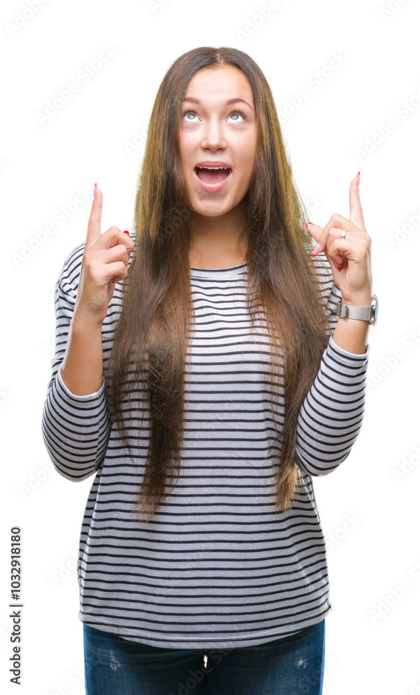 Young beautiful caucasian woman over isolated background amazed and surprised looking up and pointing with fingers and raised arms. Young beautiful caucasian woman over isolated background amazed and surprised looking up and pointing with fingers and raised arms.