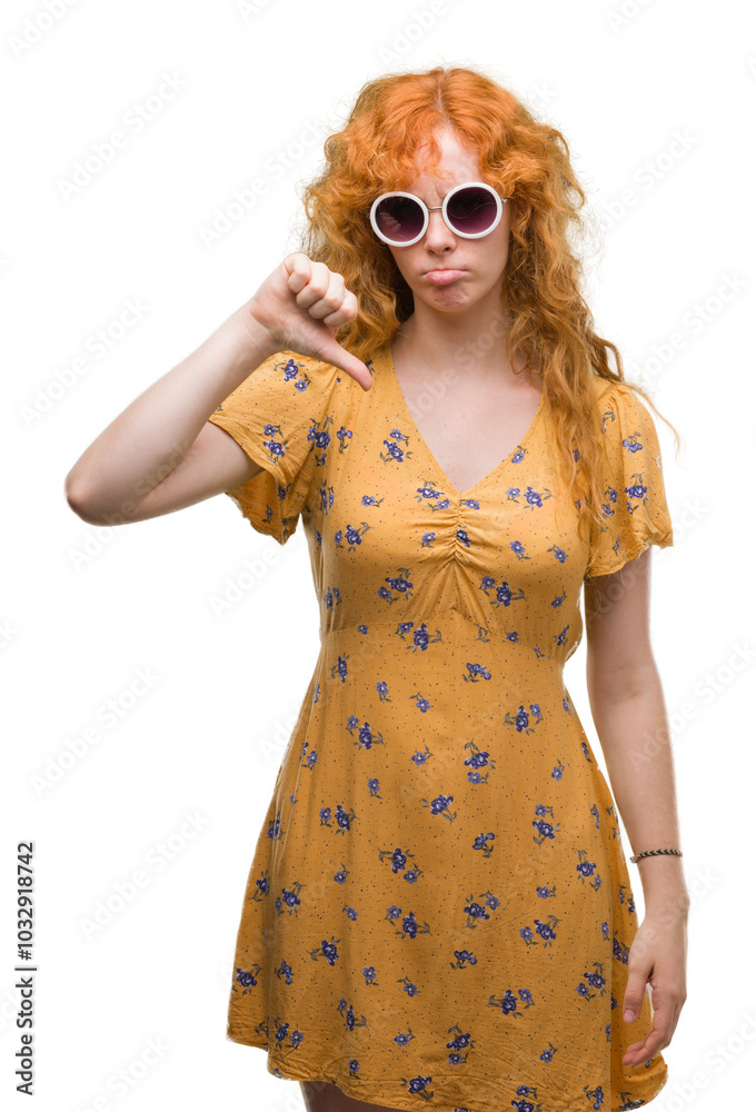 Young redhead woman wearing sumer outfit and sunglasses with angry face, negative sign showing dislike with thumbs down, rejection concept Young redhead woman wearing sumer outfit and sunglasses with angry face, negative sign showing dislike with thumbs down, rejection concept