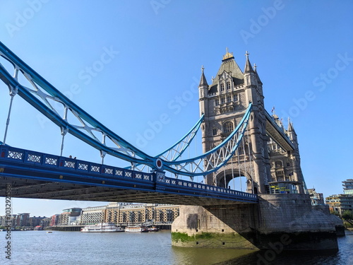 London, UK - 2023.07.02: Side view of Tower Bridge with Queen Elizabeth II Silver Jubilee repainting of blue and white over River Thames under a clear blue sky with sunlight coming from the left