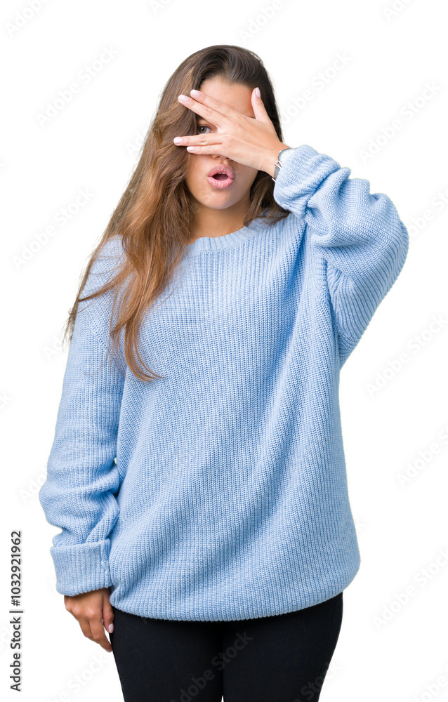 Young beautiful brunette woman wearing blue winter sweater over isolated background peeking in shock covering face and eyes with hand, looking through fingers with embarrassed expression.