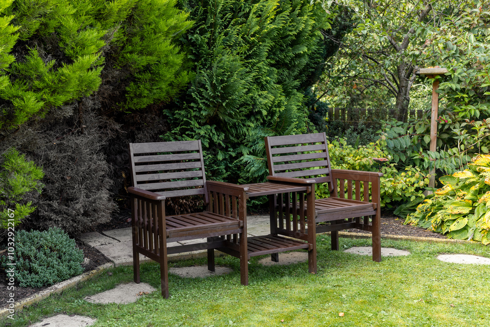 Two seat wooden garden bench set with table top on grass lawn in lush green garden Two seat wooden garden bench set with table top on grass lawn in lush green garden
