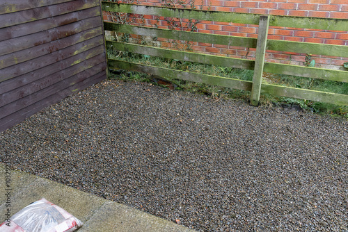 Gravel-covered area beside wooden fence and house wall in domestic garden prepared for storing domestic waste wheelie bins