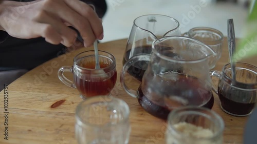 Man hand steers sugar with spoon on cup of coffee on a wooden table in a cafe or restaurant, drink americano or filter coffee from glass cup.