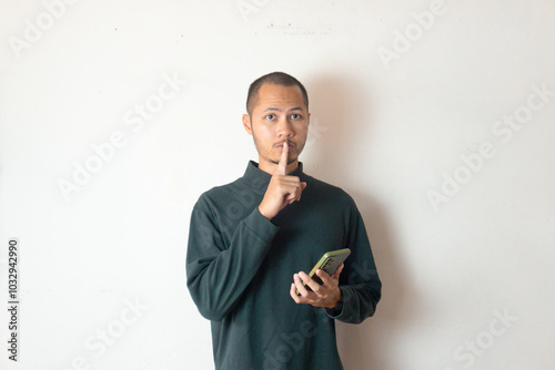 Young men wearing sweater silence gesture while holding phone isolated white photo