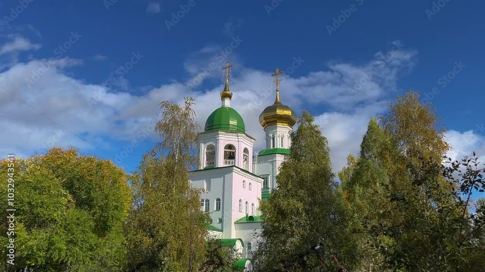 White orthodox church with green and gold domes surrounded by colorful autumn trees on a sunny day with blue sky and white clouds White orthodox church with green and gold domes surrounded by colorful autumn trees on a sunny day with blue sky and white clouds