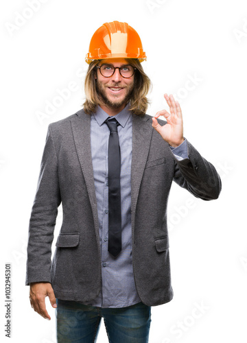 Young handsome architec man with long hair wearing safety helmet over isolated background smiling positive doing ok sign with hand and fingers. Successful expression.