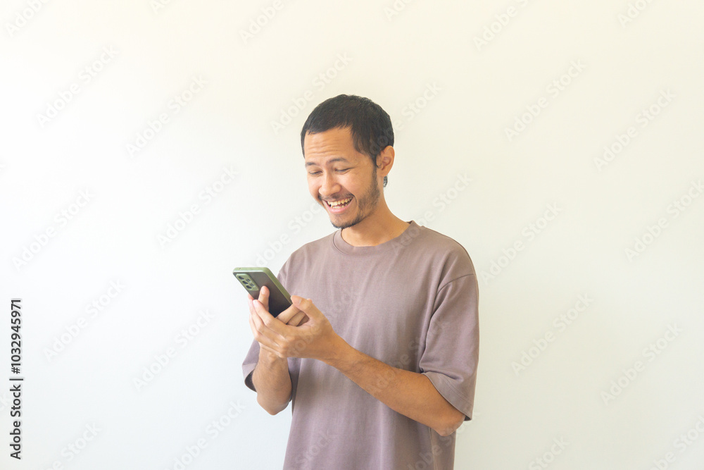 Young Asian men with purple t-shirt is holding his smartphone with happiness and smile. Positive reaction Young Asian men with purple t-shirt is holding his smartphone with happiness and smile. Positive reaction