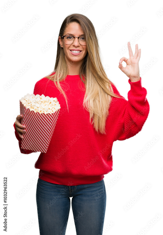 Beautiful young woman eating popcorn doing ok sign with fingers, excellent symbol Beautiful young woman eating popcorn doing ok sign with fingers, excellent symbol