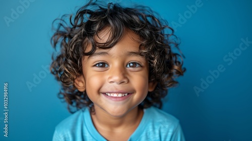 high resolution photography of an Indian boy with curly hair, wearing a blue t-shirt smiling at the camera against a blue background