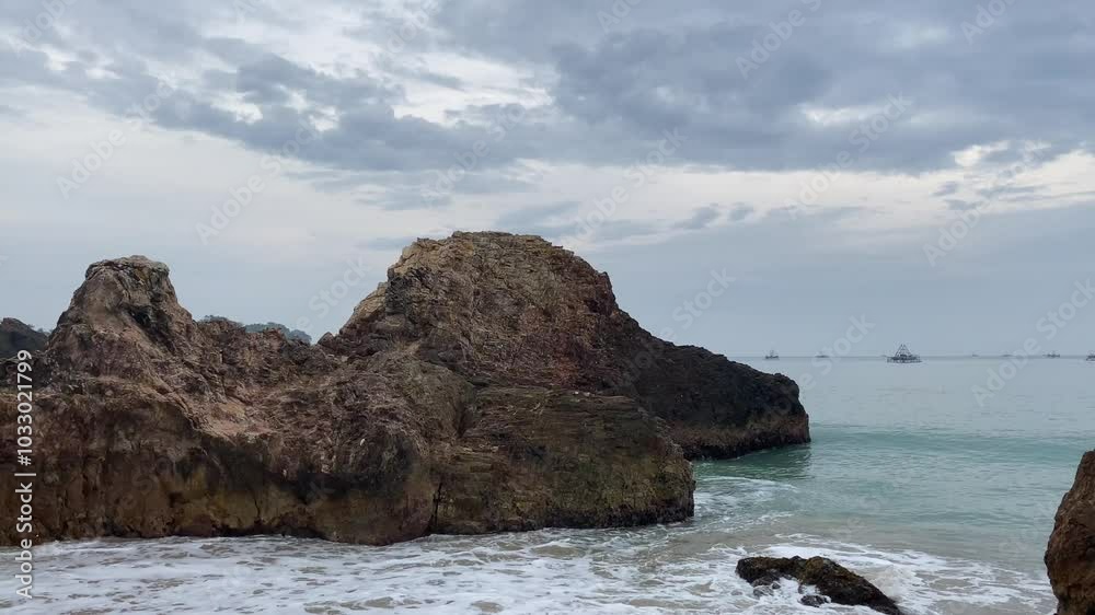 Ocean waves hitting large rock formations along a sandy beach under a cloudy sky, with calm seas in the background, perfect for coastal and nature-themed content. Ocean waves hitting large rock formations along a sandy beach under a cloudy sky, with calm seas in the background, perfect for coastal and nature-themed content.