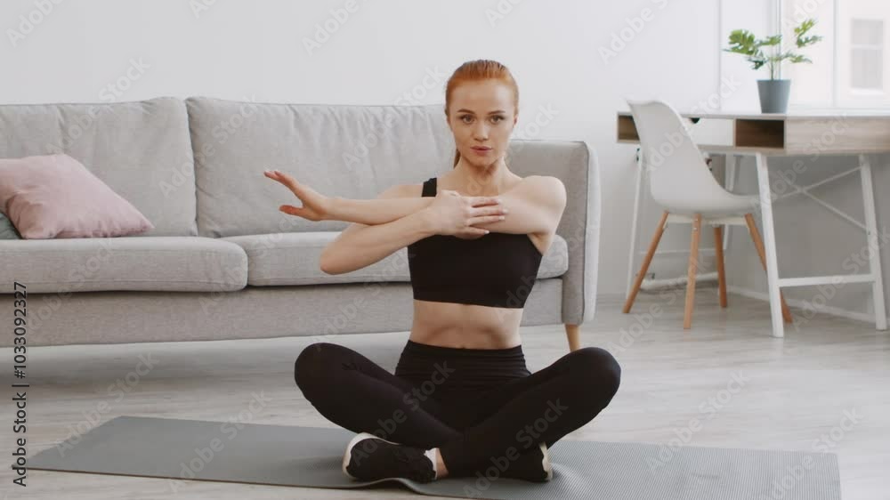 A young woman sits cross-legged on a yoga mat, performing a stretching exercise in a bright, modern living room. Natural light floods the space, enhancing the serene atmosphere. A young woman sits cross-legged on a yoga mat, performing a stretching exercise in a bright, modern living room. Natural light floods the space, enhancing the serene atmosphere.
