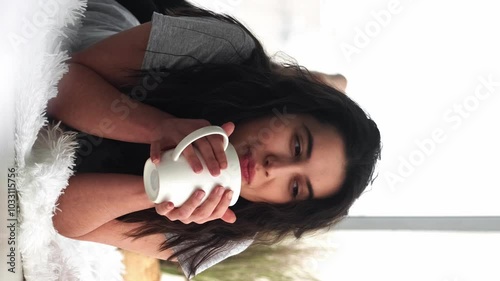 Vertical video. Morning coffee. Weekend rest. Relaxed happy dreamful woman enjoying new day with cup of tea on floor light cozy room.