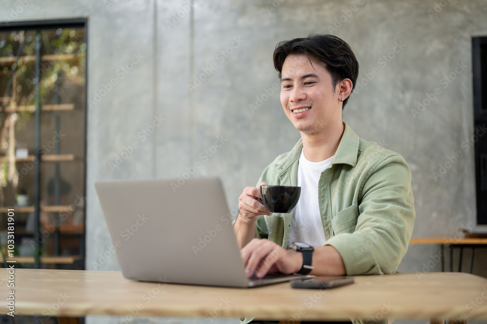 A handsome Asian man is working remotely from a coffee shop, enjoying coffee while working on laptop A handsome Asian man is working remotely from a coffee shop, enjoying coffee while working on laptop