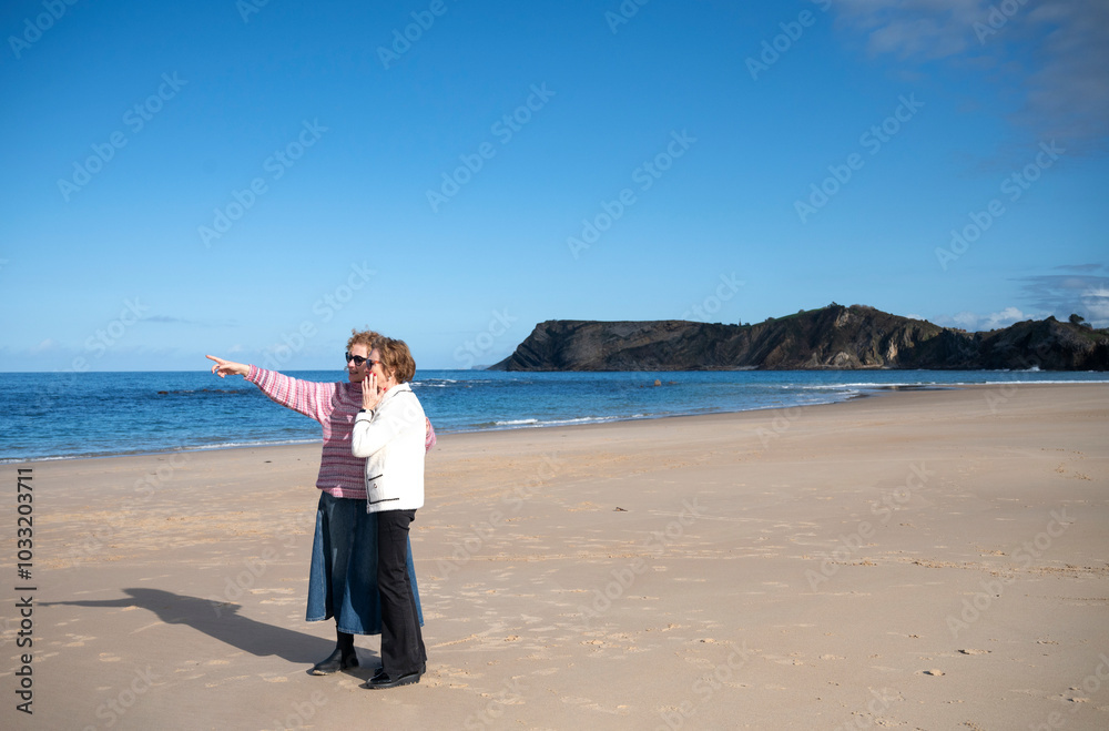 Two women, mother and daughter, standing on a beach, one pointing towards the horizon Two women, mother and daughter, standing on a beach, one pointing towards the horizon