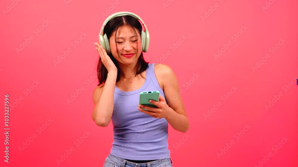 Chinese Woman Dancing with Smartphone, Enjoying Music on Vibrant Pink Background Chinese Woman Dancing with Smartphone, Enjoying Music on Vibrant Pink Background