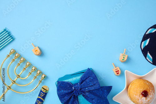 Flat lay composition for Hanukkah on blue background. Top view Chanukah Jewish accessories, gold menorah, mezuzah, candles, jelly donut, kippah, dreidels, gift box photo