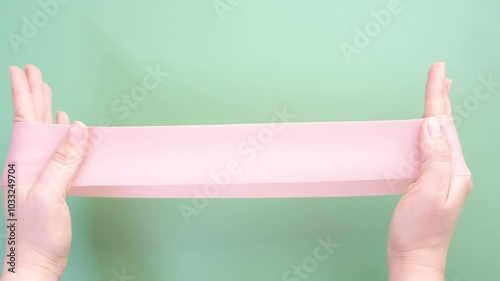 Hands stretching fitness elastic band on green background close-up.