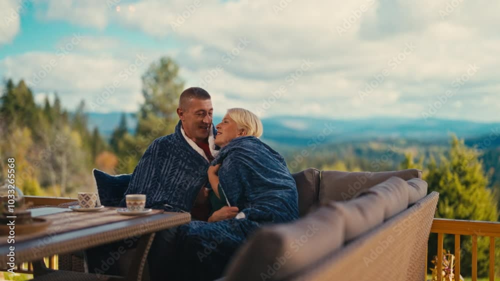 Caucasian couple in their 40s enjoying cozy atmosphere outdoors on a terrace, wrapped in a blanket with coffee cups on the table, surrounded by autumn scenery. Concept of romance, love, warmth, bond Caucasian couple in their 40s enjoying cozy atmosphere outdoors on a terrace, wrapped in a blanket with coffee cups on the table, surrounded by autumn scenery. Concept of romance, love, warmth, bond