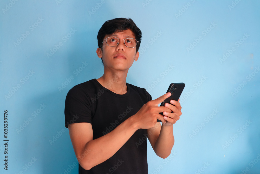 Young Asian man thinking about something while holding a mobile phone Young Asian man thinking about something while holding a mobile phone