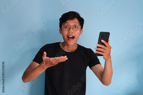 Young asian man wearing black t-shirts showing wow expression while holding mobile phone photo