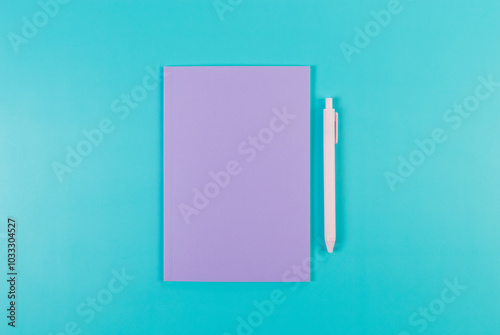 Top view of purple notebook, pink pen on blue background. School, office wallpaper. Flat lay, copy space.