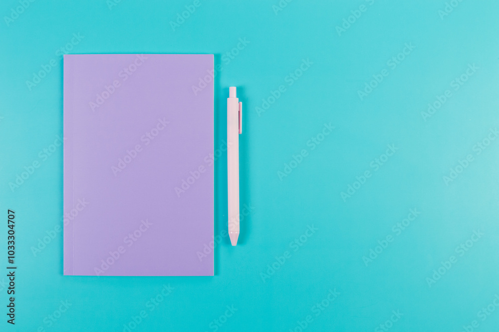 Top view of purple notebook, pink pen on blue background. School, office wallpaper. Flat lay, copy space.