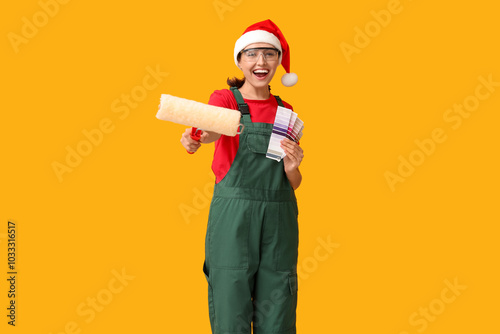 Beautiful female painter in Santa hat with roller and color palettes on yellow background photo