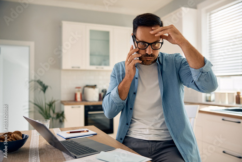 Distraught man making  phone call while working on laptop at home.